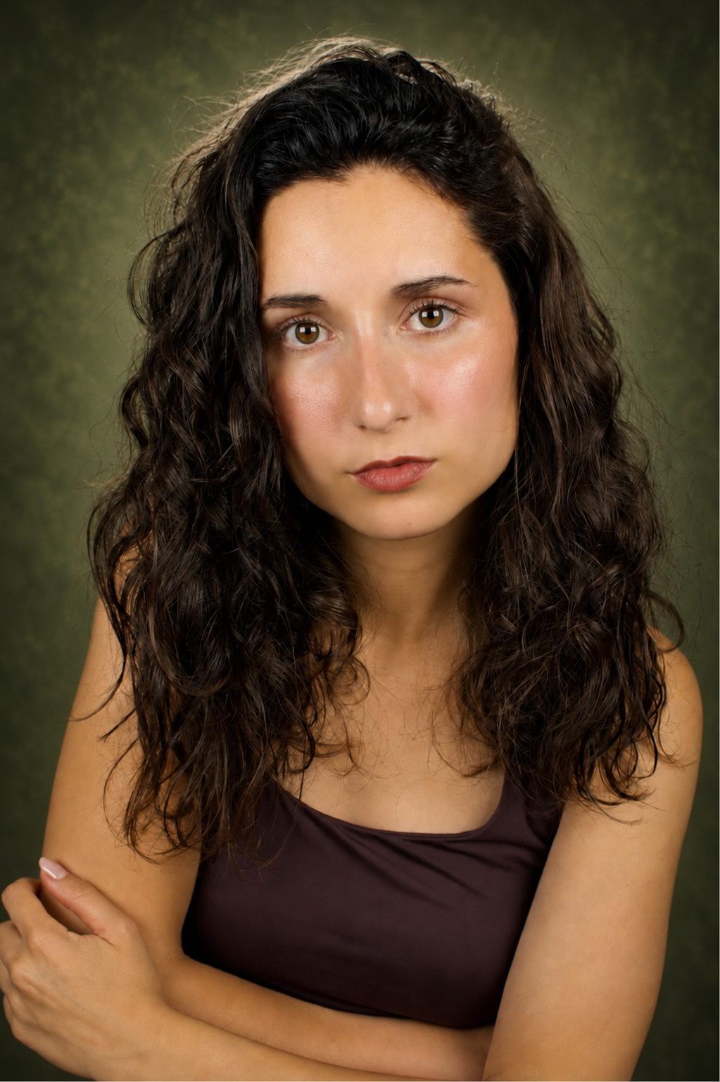 Jessica Curado with long natural curls in a dark vest against an olive backdrop, unsmiling and watchful.
