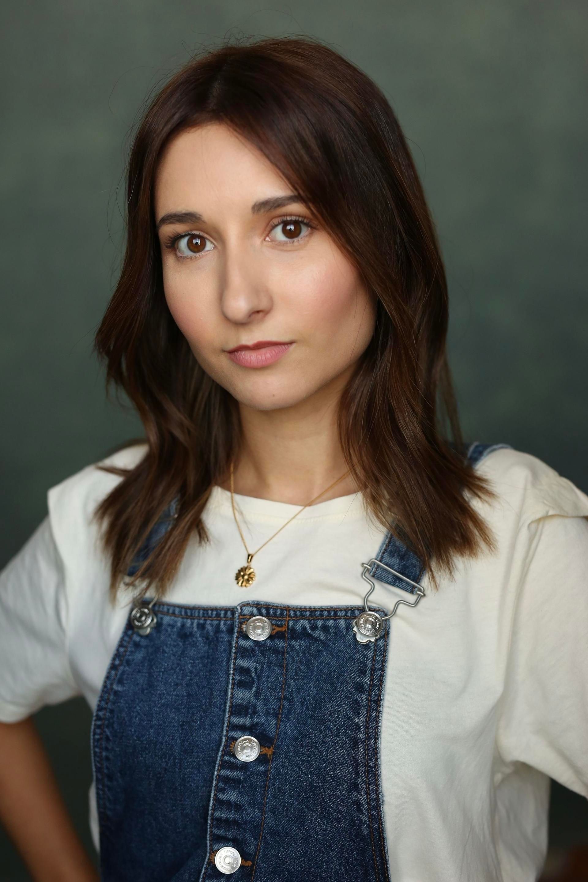 Jessica Curado in denim dungarees and a cream T-shirt with a small gold pendant, a soft, open expression.
