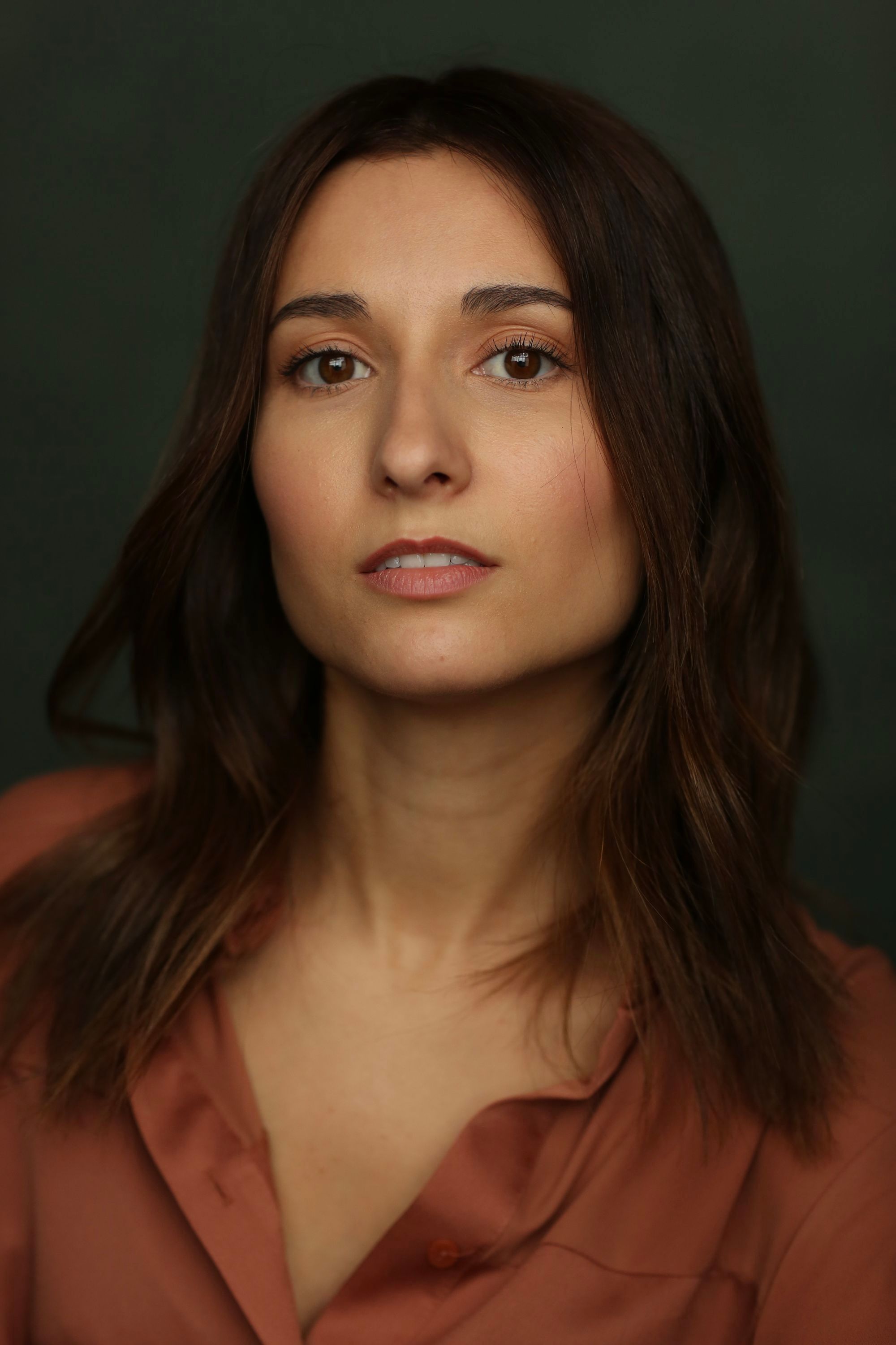 Jessica Curado in a rust-coloured shirt against a dark green backdrop, looking straight into the lens.