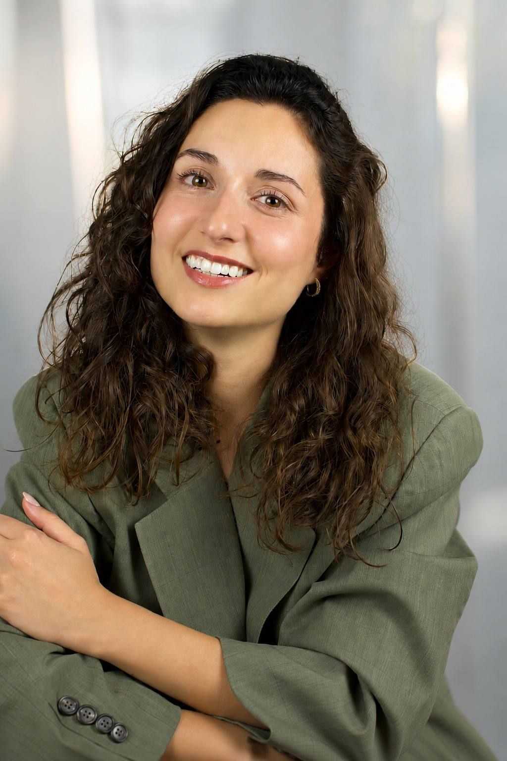 Jessica Curado smiling broadly in a sage-green blazer, curly hair loose over her shoulders.