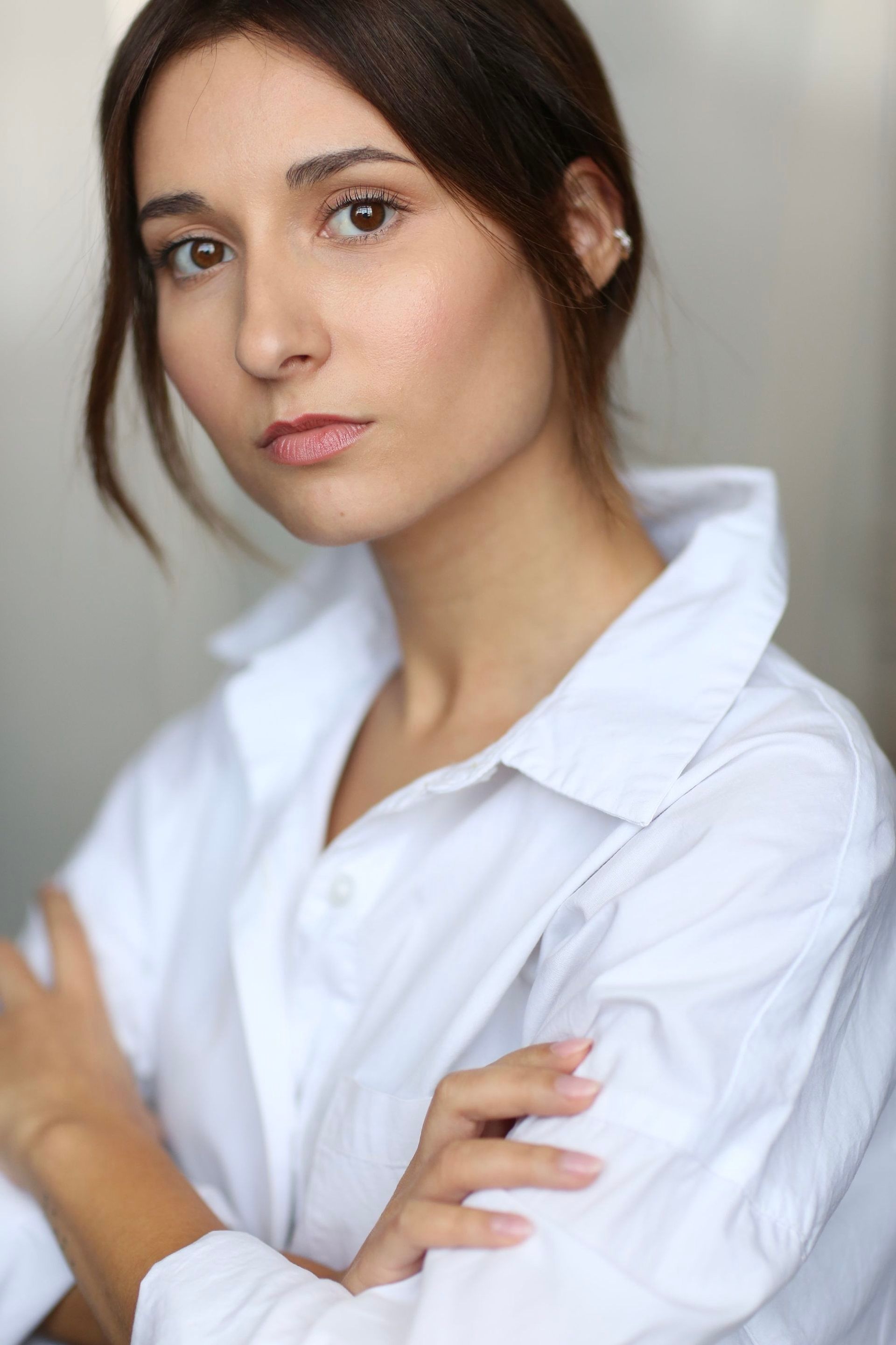 Jessica Curado in an oversized white shirt, hair pulled back, arms folded, with a level, guarded gaze.